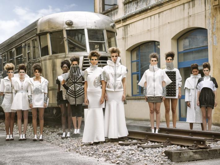 A fashion picture of twelves models dressed in silver and white, standing near an abandoned train station.