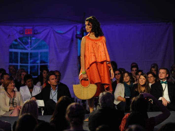 A model, dressed in an orange outfit, is posing on the catwalk.